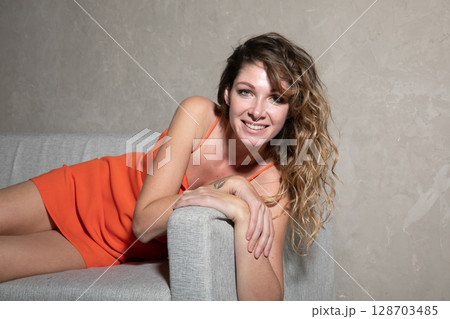woman in orange summer dress sitting on sofa and smiling woman in orange summer dress sitting on sofa and smiling 128703485