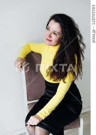 woman in yellow and black dress sitting on chair by window in white room woman in yellow and black dress sitting on chair by window in white room 128703563