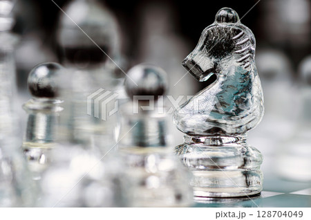 transparent glass chess on dark background, selective focus on horse piece, close-up transparent glass chess on dark background, selective focus on horse piece, close-up 128704049