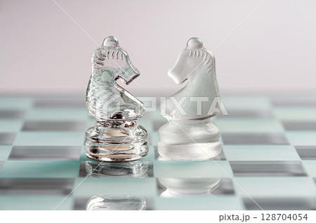 two opponent glass chess knights on a glass chess board, light background, closeup 128704054