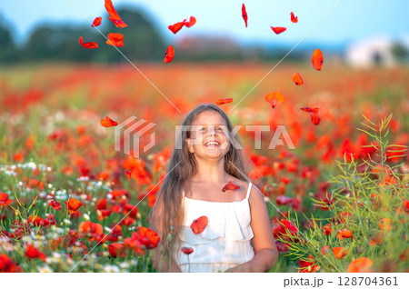 cute girl wearing white dress in summer blooming poppy field playing under evening sun 128704361