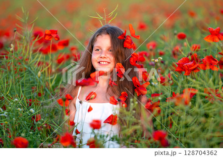 cute girl wearing white dress in summer blooming poppy field walking under evening sun 128704362