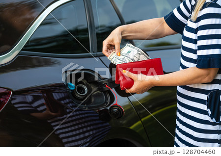 a woman counts money standing at an open fuel tank, the concept of rising fuel prices, closeup 128704460
