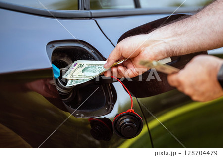 hand of man that puts money into the tank of car, close up, concept of expensive fuel, fuel crisis hand of man that puts money into the tank of car, close up, concept of expensive fuel, fuel crisis 128704479