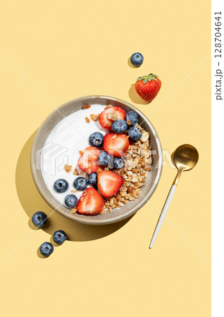 Natural yogurt with granola, blueberry and strawberry in a bowl on a bright yellow background 128704641