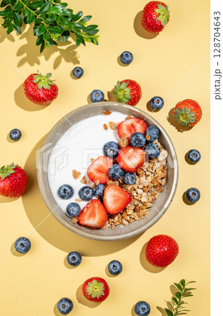 Natural yogurt with granola, blueberry and strawberry in a bowl on a yellow background Natural yogurt with granola, blueberry and strawberry in a bowl on a yellow background 128704643