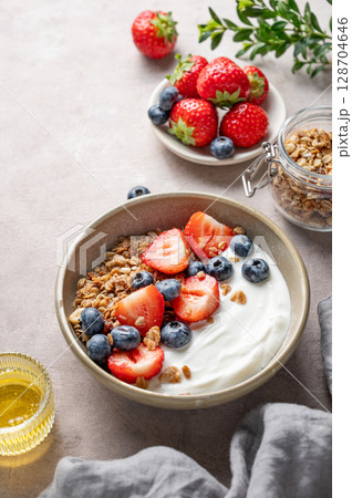 Natural greek yogurt with granola, blueberry and strawberry in a bowl on a light background 128704646