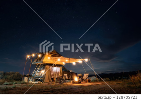 Cozy rooftop tent lit by string lights under a starlit sky, offering an adventurous camping escape with scenic nighttime views 128705723