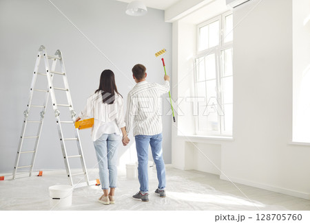 Happy to repair new own flat painting walls in light color, married young couple enjoying moving Happy to repair new own flat painting walls in light color, married young couple enjoying moving 128705760