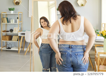 Obese woman mirror looking with excessive belly visceral fat at home trying on jeans, overweight  128705779