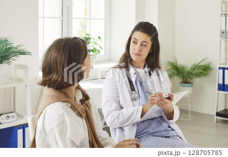 Doctor holding report file with appointment and listening her woman patient in clinic. Doctor holding report file with appointment and listening her woman patient in clinic. 128705785