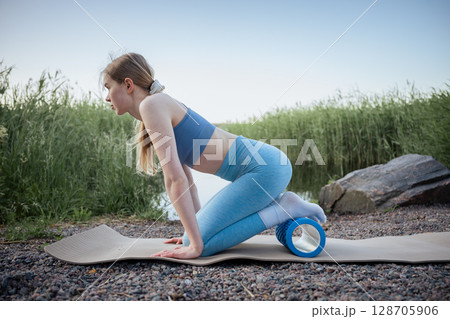 Woman using massage roller in outdoor workout near lake in summer 128705906