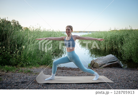Young woman doing yoga exercise outdoors near lake in summer Young woman doing yoga exercise outdoors near lake in summer 128705913