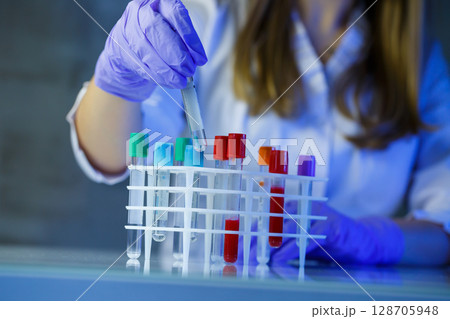 A medical professional, laboratory assistant, doctor performs an analysis in a laboratory, uses test tubes, a pipette and a petri dish for the presence of bacteria in the human body 128705948