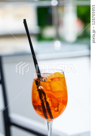 Refreshing light delicious summer aperol cocktail with ice and orange in a glass goblet, soft drink with straws for girls 128705955