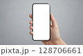 A hand holding a modern smartphone with a blank white screen against a neutral backdrop. 128706661