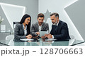 Three business professionals collaborating, analyzing data on a tablet device, discussing strategy. 128706663