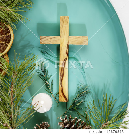 Wood cross laying on a green marble podium with fir branches, cones, candle and dry oranges on a white background. Christmas holidays. Christian religion card. Flat lay 128708484