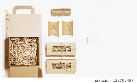Eco friendly packaging concept. Cardboard boxes with shredded paper inside, paper bag and small gift boxes for packaging goods from online stores and delivery on white background with copy space 128708487