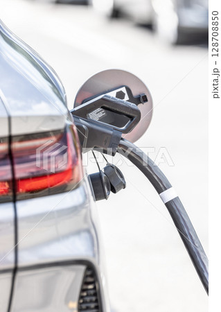 Focus closeup electric vehicle plugged in with EV charger device from blurred background of public charging station powered by renewable clean energy for progressive eco-friendly car concept 128708850