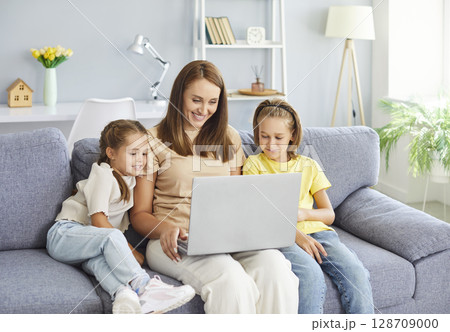 Happy young mother with two kids sitting on sofa using modern laptop together. Happy young mother with two kids sitting on sofa using modern laptop together. 128709000