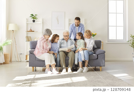 Large Happy Family Looking Through Photo Album Together On Sofa At Home 128709148