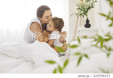 Loving mother gently kisses her daughter on forehead, filling morning with warmth and love. Loving mother gently kisses her daughter on forehead, filling morning with warmth and love. 128709151
