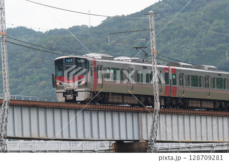 【広島・可部線】緑の山々を背に鉄橋を走るJR227系電車（Red Wing） 128709281