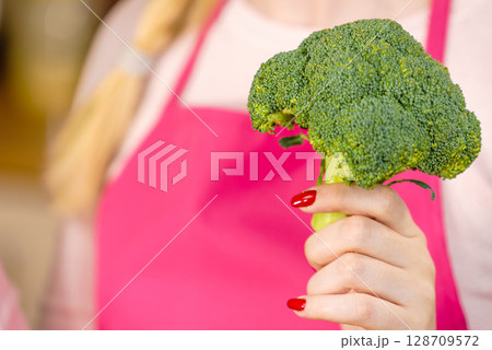 Woman in kitchen holding green fresh broccoli. Woman in kitchen holding green fresh broccoli. 128709572