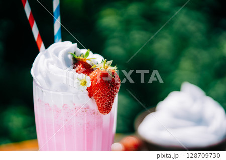 Still life - amazing strawberry milkshake cocktail with straw on nature backdrop 128709730