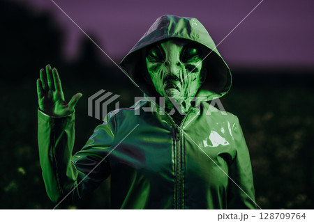 Spooky alien waving hello, hi, salute in field under green neon light. Scary mask, vinyl smooth Spooky alien waving hello, hi, salute in field under green neon light. Scary mask, vinyl smooth 128709764