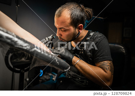 Man tattoo master with dreadlocks showing process creation tattoo, female body  128709824