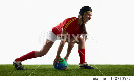Female rugby player in action pose on grassy field with helmet and ball Female rugby player in action pose on grassy field with helmet and ball 128710577