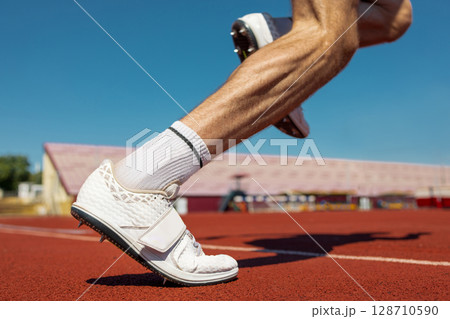 Close-up of athlete's legs starting on running track in sunlight 128710590