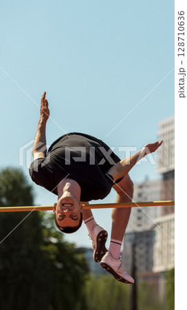 Athlete midair executing high jump at outdoor track and field event Athlete midair executing high jump at outdoor track and field event 128710636