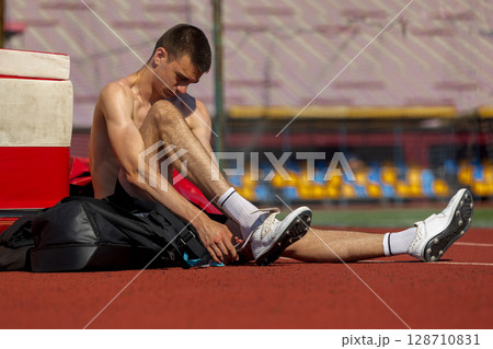 Athlete lacing up shoes on running track under sunny sky 128710831