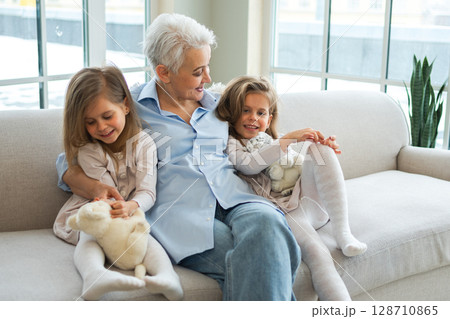 Happy family at home. Two little girls sisters twins grandmother enjoying time together. Good time at home. Grandma granddaughters child kids emotional bonding hugging together. Family generations 128710865
