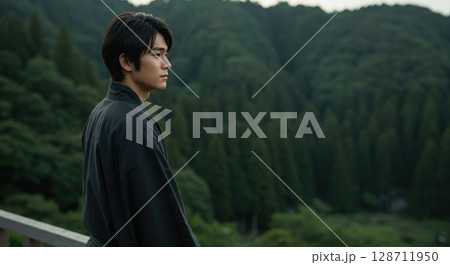 Young japanese man in a black kimono looking at the beautiful green mountain forest landscape 128711950