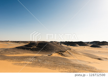 Ash-covered hills in Egypt's Black Desert under a clear sky, scenic and remote landscape. Volcanic Ash-covered hills in Egypt's Black Desert under a clear sky, scenic and remote landscape. Volcanic 128712500