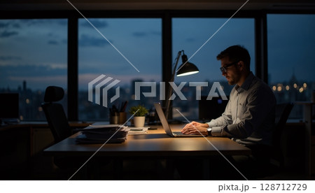 Focused professional working late at night in modern office space with city skyline view 128712729