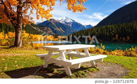 An autumn mountain landscape with a serene lake, a lone bench, and reflections of the scenic sky 128712878