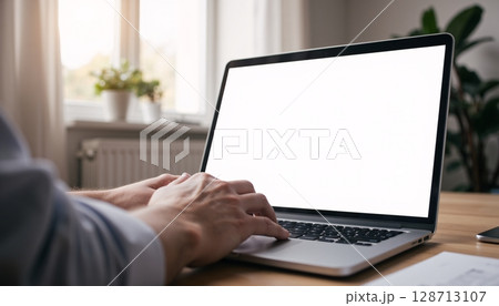 Person Using Laptop at Home Office with Blank Screen and Natural Light from Window 128713107