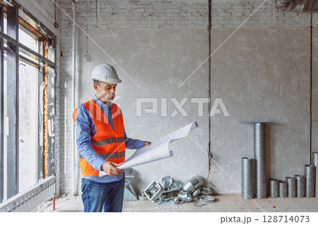 Construction worker analyzes blueprints in a newly built office space during daylight hours 128714073