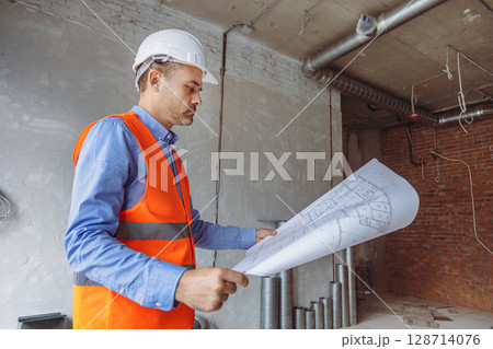 Construction manager reviewing plans in a partially finished building with exposed walls and pipes Construction manager reviewing plans in a partially finished building with exposed walls and pipes 128714076