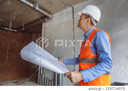 Construction manager reviewing plans in a partially finished building with exposed walls and pipes Construction manager reviewing plans in a partially finished building with exposed walls and pipes 128714078