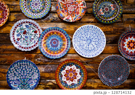 Colorful decorative ceramic plates on rustic wooden wall display 128714132
