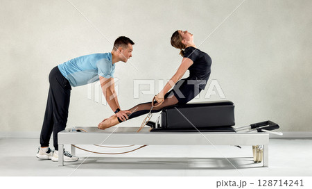 Fitness Instructor Assisting Woman in Pilates Exercise on Reformer Machine Fitness Instructor Assisting Woman in Pilates Exercise on Reformer Machine 128714241