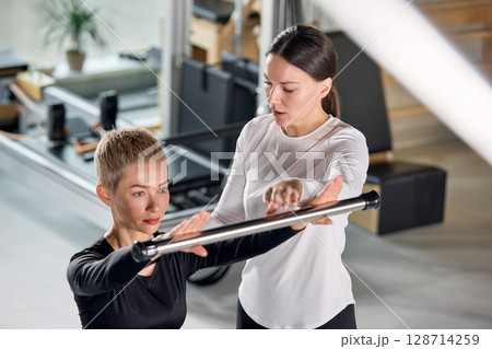 Fitness trainer assisting a client with equipment during a gym workout 128714259