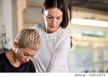 Fitness instructor assisting client during exercise in a gym setting Fitness instructor assisting client during exercise in a gym setting 128714275