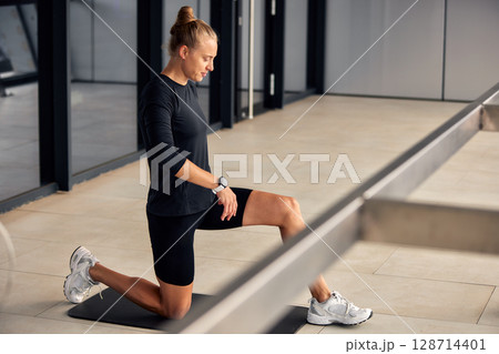 Woman Performing Stretching Exercise Indoors on Mat with Focused Expression Woman Performing Stretching Exercise Indoors on Mat with Focused Expression 128714401